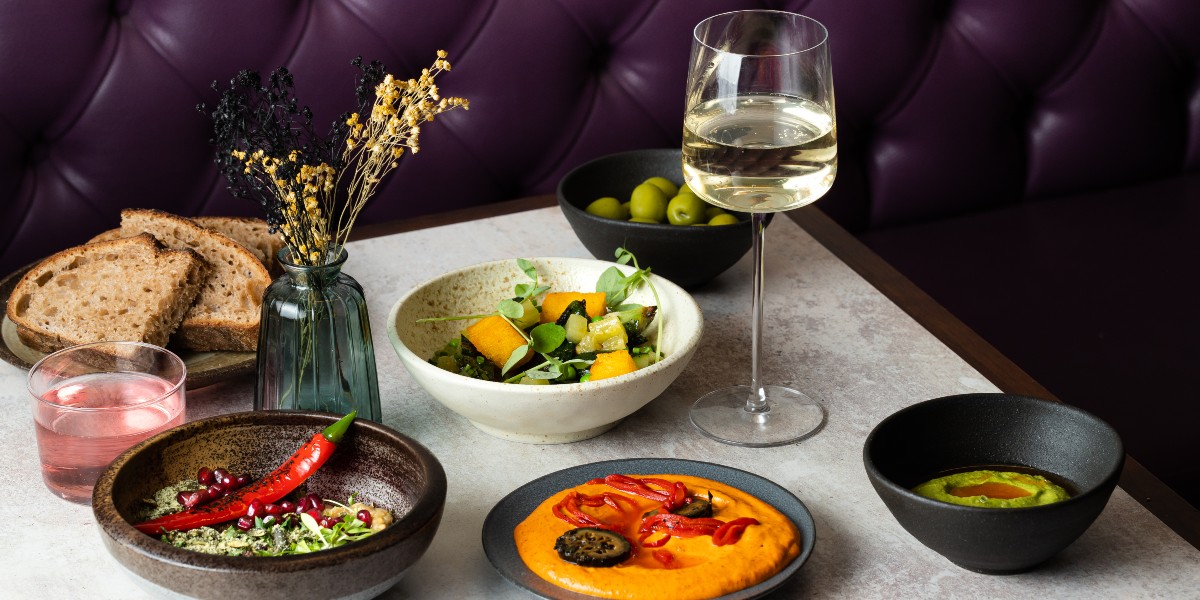 Table with small plates of colourful food, a glass of white wine and a pink cocktail
